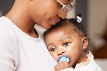 Shes getting tired now. Shot of an adorable baby girl sucking a dummy while being held by her mother at home.