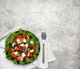 Greek salad with tomatoes, cucumbers, olives, feta cheese, herbs in a plate, fork. Top view, flat lay.