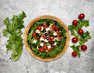 Greek salad with tomatoes, cucumbers, olives, feta cheese, herbs in a plate on a light background. Top view, flat lay. 
