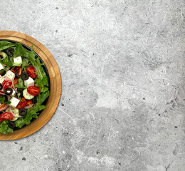 Greek salad with tomatoes, cucumbers, olives, feta cheese, herbs in a plate on a light background. Top view.