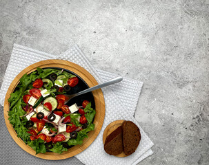 Greek salad with tomatoes, cucumbers, olives, feta cheese, herbs in a plate, fork, bread. Light background. Flat lay. 