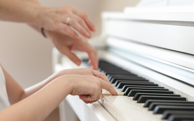 Learning to play the piano, the hands of a child and a teacher on the keys of a white piano