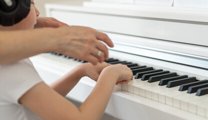 Fototapeta premium Learning to play the piano, a child with headphones on his head and the teacher's hands on the keys of a white piano