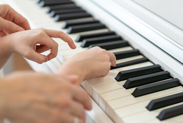 Fototapeta premium Learning to play the piano, the hands of a child and a teacher on the keys of a white piano