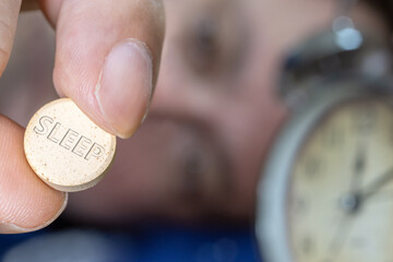 Man lying in bed taking sleeping pill after midnight, close up