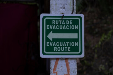 Sign in Spanish and English evacuation route with a direction arrow. Safety, danger, natural disaster concept.