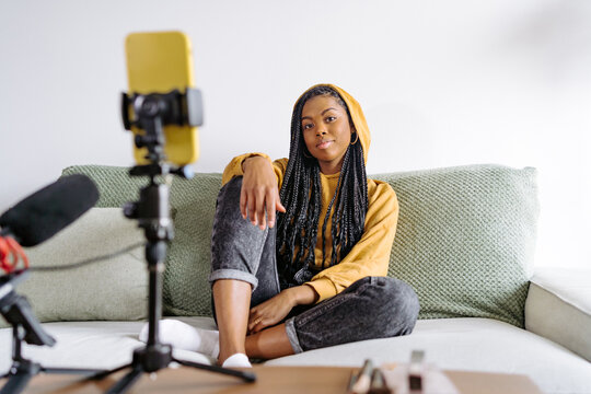 Content black woman in hoodie recording video on sofa