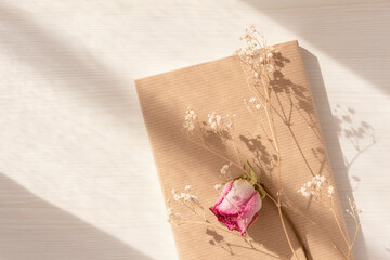 Dried flowers of pink roses and hazel flowers attached to a book on a table at twilight
