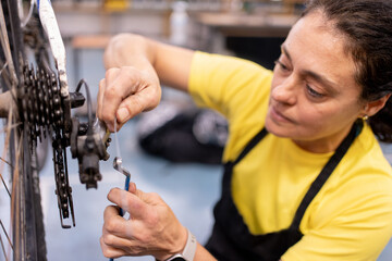 woman fixing bike rear wheel change, bike hung with chain for repair and adjustments. Girl in black apron and colorful yellow t-shirt.