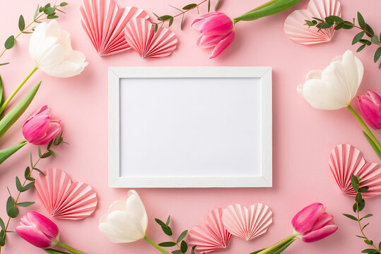 Mother's Day concept. Top view photo of photo frame tulips and origami paper hearts on isolated pastel pink background with copyspace