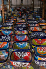 Close up of many colorful ceramic snack and sauce bowls arranged in rows at a local souvenir craft store, selective focus.