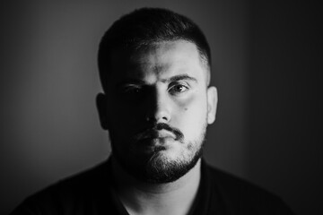 Grayscale portrait of a serious young Caucasian male with a shadow falling on his face