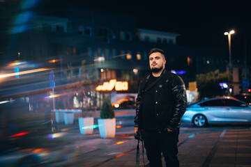 Young Caucasian male in a black outfit walking on a street at night