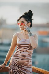 Vertical shot of a sexy Caucasian white woman in a silk dress and sunglasses on the balcony