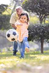 Little girl with grandfather playing football in park