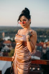 Vertical shot of a sexy Caucasian white woman in a silk dress and sunglasses on the balcony