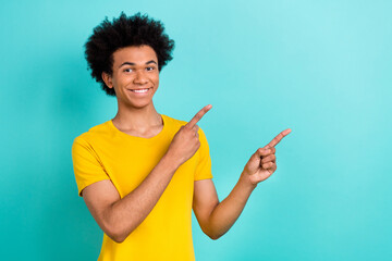 Portrait of funny guy with afro hairdo wear yellow t-shirt look directing at offer empty space isolated on vibrant teal color background