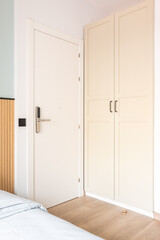 View of white front doors with electronic digital lock next to wardrobe and bed in hotel room. Concept of a modern security and protection system