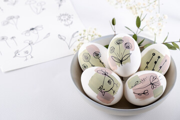 Bowl with modern creative trendy  hand painted easter egg in spring flowers on white background.  Homemade tradition Easter ideas. Greeting card