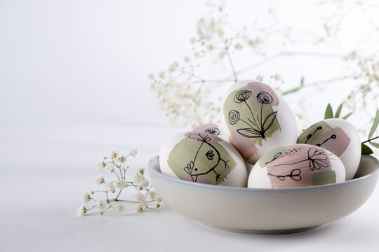 Bowl with modern creative trendy  hand painted easter egg in spring flowers on white background.  Homemade tradition Easter ideas. Greeting card