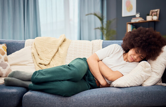 Black Woman, Lying On Sofa With Stomach, Menstruation Or Pain Holding Abdomen In Home Living Room. Woman, Lounge And Hurt With Sore Tummy, Constipation Or Bloated With Cramps, Period Or Belly Ache