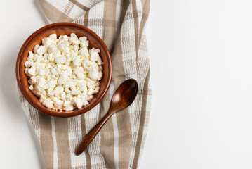 Fresh farm cottage cheese in a clay bowl with a wooden spoon on a napkin on a white background, top view with copy space