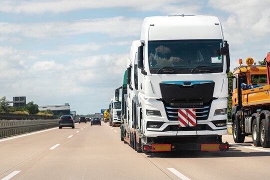 Back View Of Semi-trailer Flatbed Vehicle Deliverying Many New Electric Trucks Sale Automotive Dealer From Factory Plant On Highway Interstate Road. New Business Cargo Transport Fleet Export Import