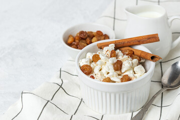 Breakfast with natural cottage cheese with raisins and cinnamon in bowl and creamer with milk on napkin close up
