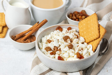 Breakfast with natural cottage cheese  with cookies, raisins and cinnamon in bowl, coffee and creamer with milk on napkin close up