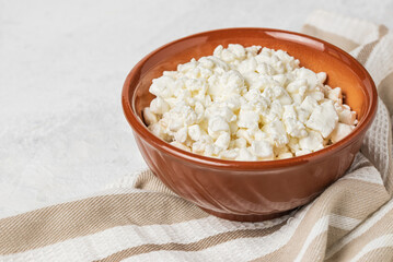 Clay bowl with fresh natural cottage cheese on  stripped napkin on a light background close up