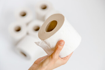 Closeup of person holding a roll of toilet paper in his hand and in the background a pile of other rolls. Concept of concern for sustainability, and environmental awareness in the use of resources.