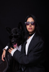 Portrait of young woman with her Belgian Shepherd on a black background. Both wearing sunglasses. Funny dog photography