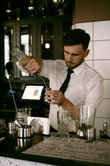 A young man bartender works in a bar made a cocktail.