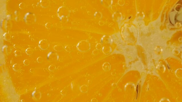 A slice of ripe orange in water bubbles on an orange background.