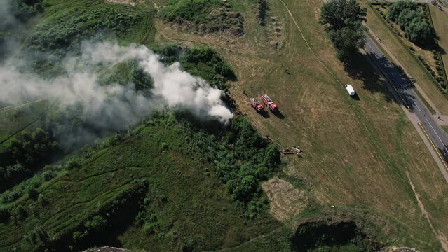 Aerial view of two fire engines are standing near center of ignition and clouds of smoke in wasteland next to road