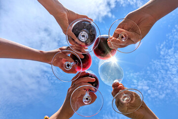 Cheers!! toasting with wineglasses of wine as seen from below against blue sky with sunlight
