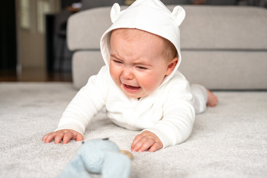 Authentic lifestyle photo of infant baby girl seven months old which lying on floor at home and crying because feeling sadness, hungry or pain
