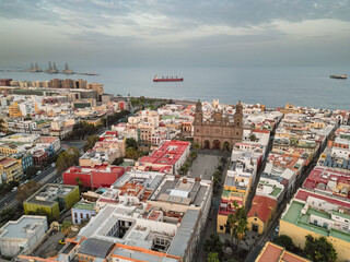 Aerial view of cathedral, square and rooftops in old town with view of the ocean and a ship in the background in the city of Las Palmas de Gran Canaria, Spain