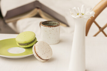 Cup of tea or coffee, macaroons, a book on white table near modern sofa indoors. Home interior.