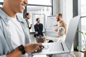 Obraz premium Smiling businessman pointing at flip chart near colleagues during presentation in office.