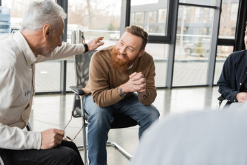 Fototapeta premium Mature man comforting smiling person with alcohol addiction in rehab center.