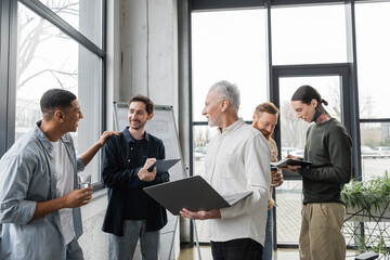 Positive interracial business people with laptop and clipboard talking during training in office.