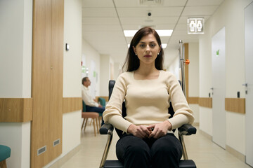 Serious young woman sitting in a wheelchair in medical center
