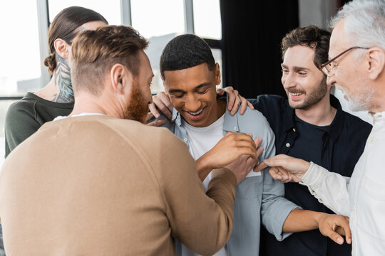 Positive people hugging african american man during alcoholics meeting in rehab center.
