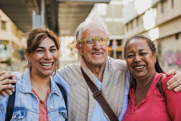 Multiracial senior friends smiling on camera while waiting at the tram station in the city