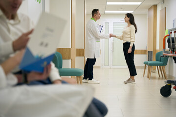 Background, a handshake between a doctor and a patient in a hospital corridor