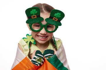 Close-up portrait adorable cute little Irish girl, wearing stylish carnival goggles and clover...