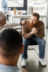 Middle aged man calming tattooed person with alcohol addiction during therapy in rehab center.