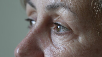 A thoughtful senior woman with contemplative expression macro eyes close up. One mature older female person in 70s looking at horizon daydreaming