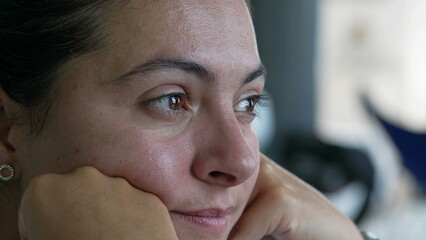 A pensive woman close up face with tearful emotion. Contemplative female person in 30s with hands in chin in thoughtful expression